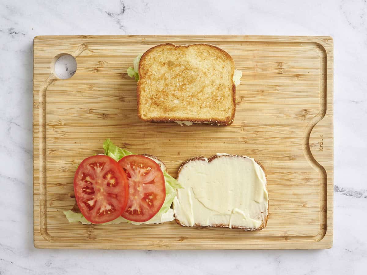 Overhead view of two BLT sandwiches on a wooden cutting board, with one open showing the lettuce and tomatoes.