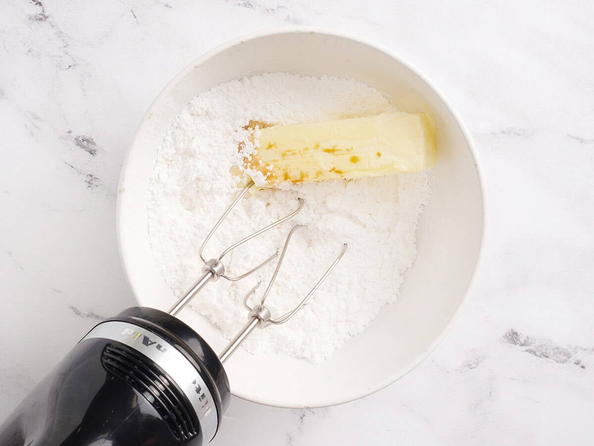 Powdered sugar and butter in a bowl with a hand mixer.