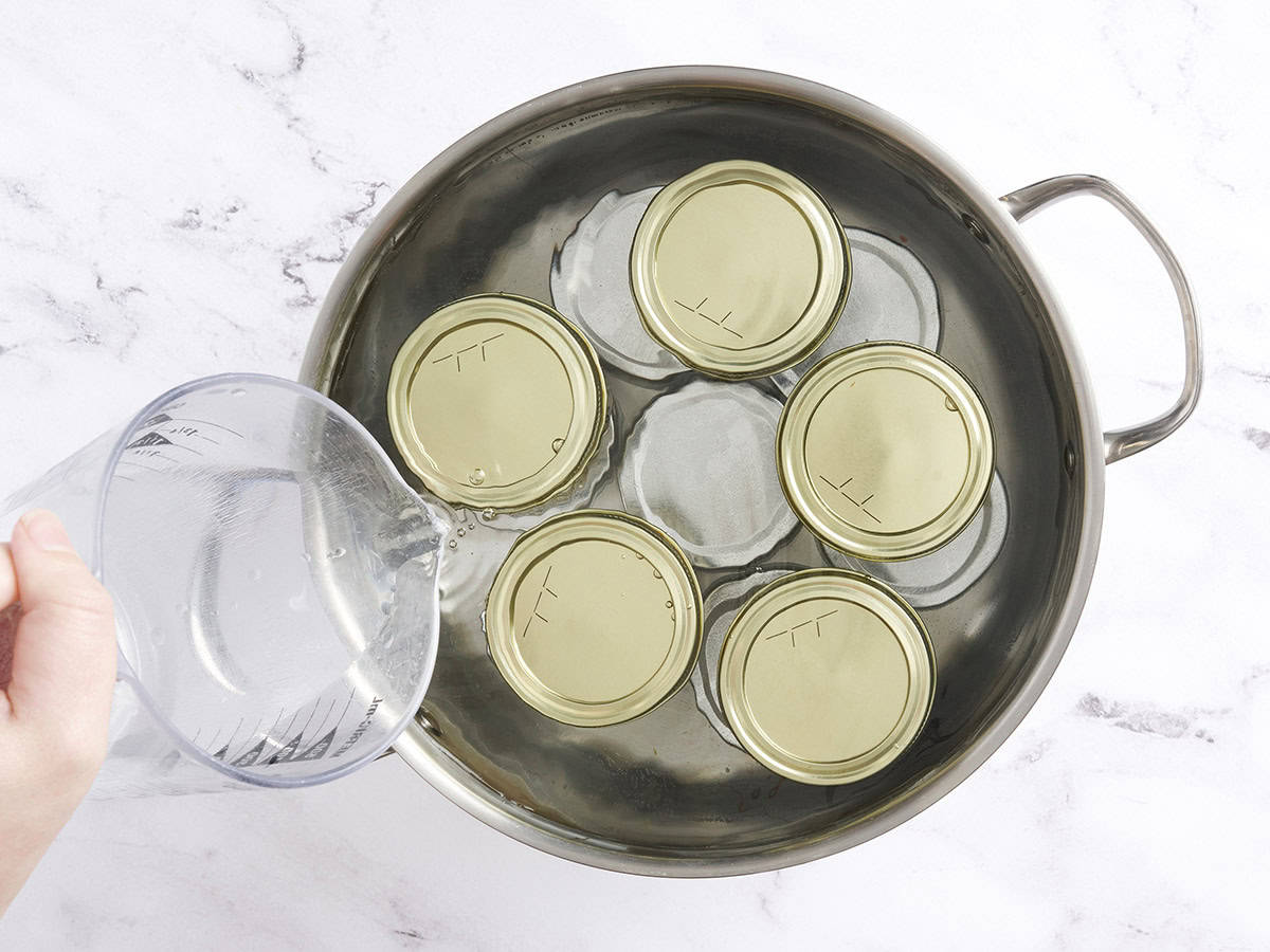 Water being poured into a saucepan of zucchini relish jars.
