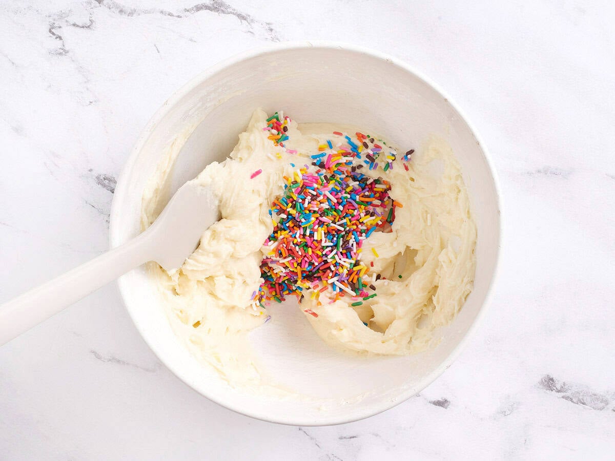 Sprinkles added to frosting in a bowl.