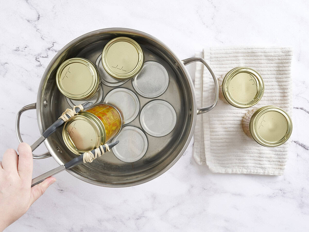 Kitchen tongs removing canned zucchini from a sauce pan.