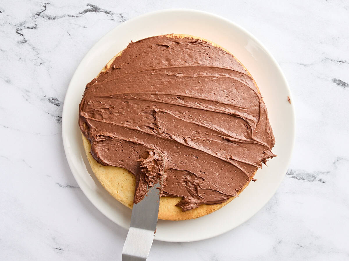 Chocolate buttercream being spread onto one layer of a homemade vanilla cake.