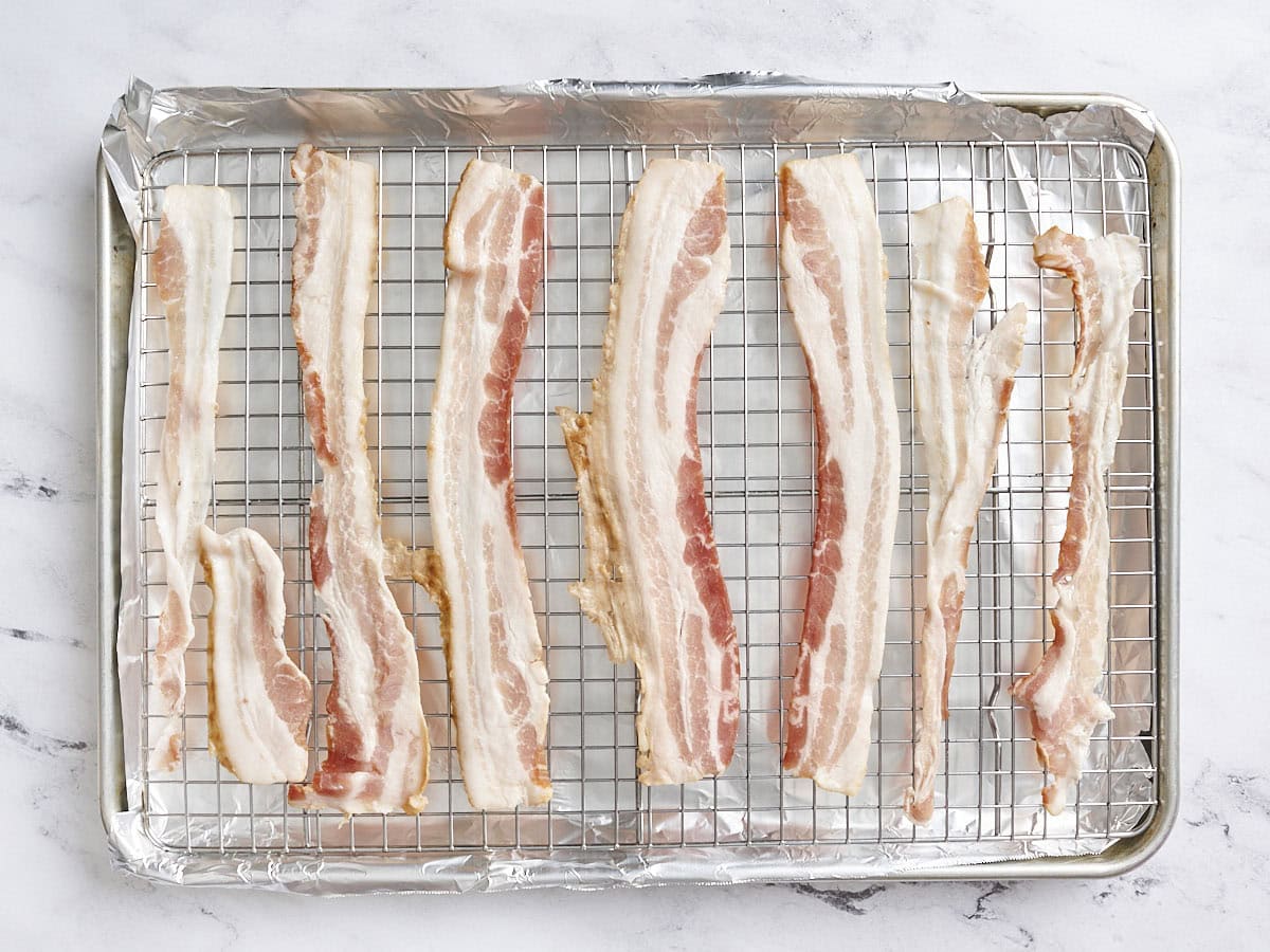 Slices of raw bacon on a baking sheet.
