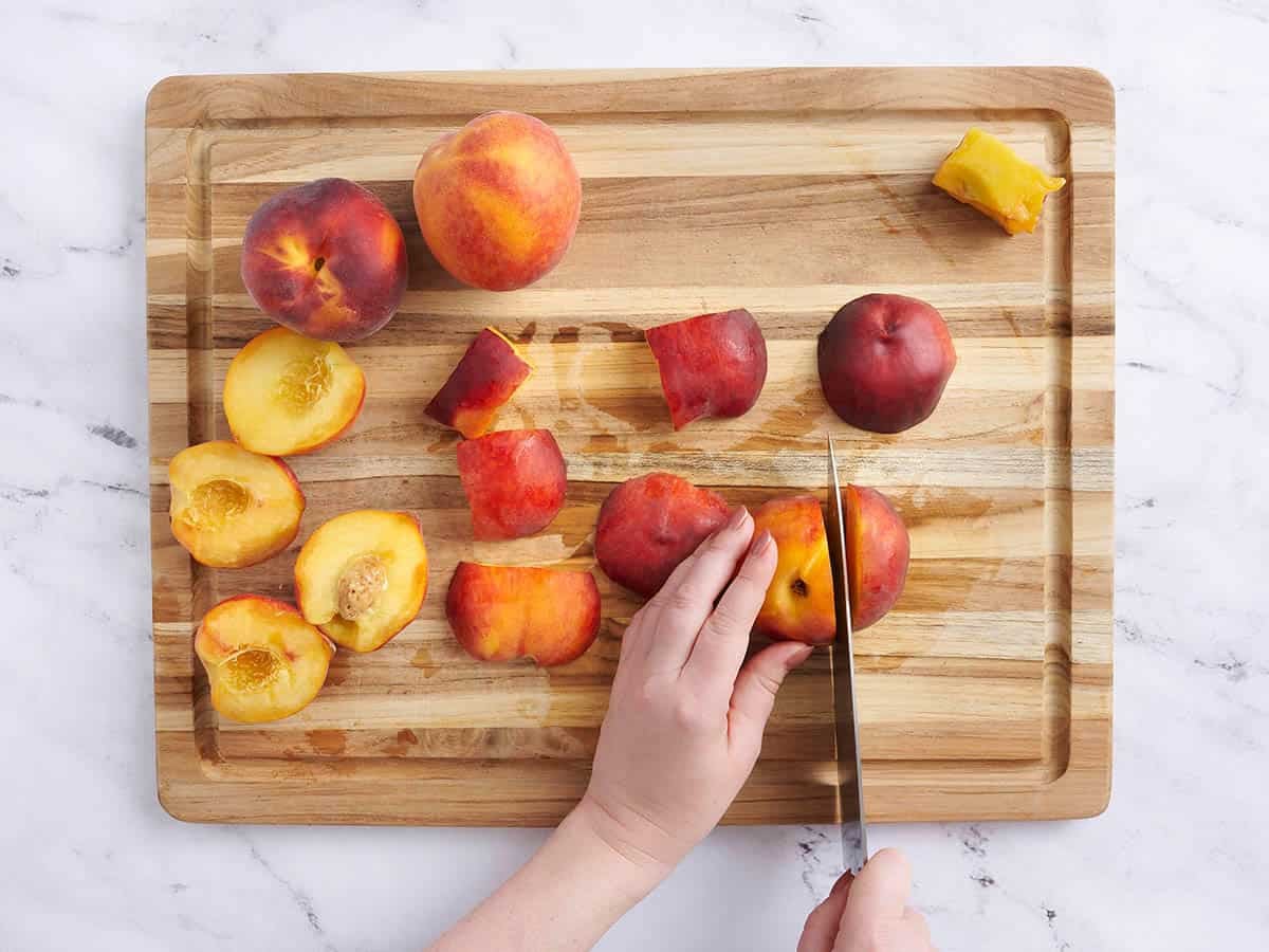 A hand cutting fresh peaches on a wooden cutting board.