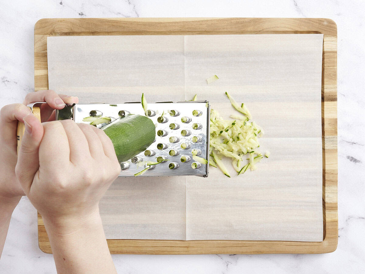A hand grating a zucchini for zucchini relish.