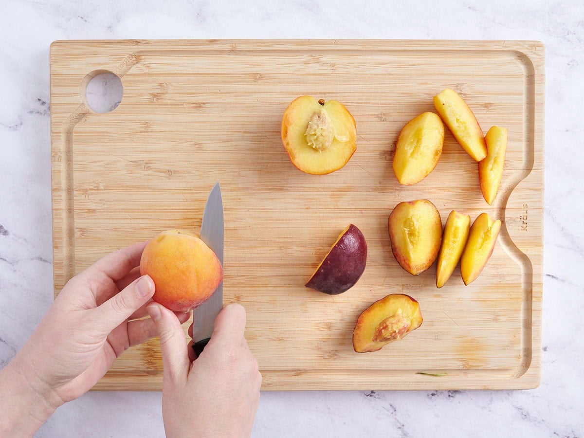 Peaches being cut into wedges on a wooden cutting board.