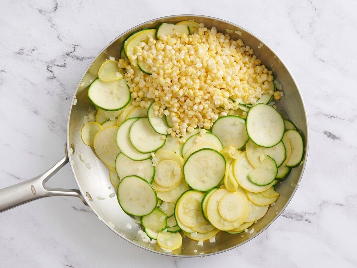 Corn kernels added to a skillet with sauteed zucchini and yellow squash.