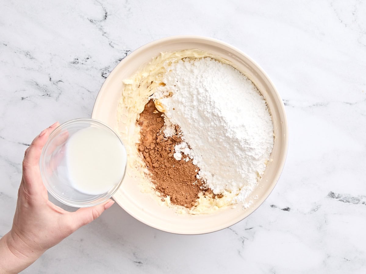 Milk being added to a bowl of cocoa powder and powdered sugar.