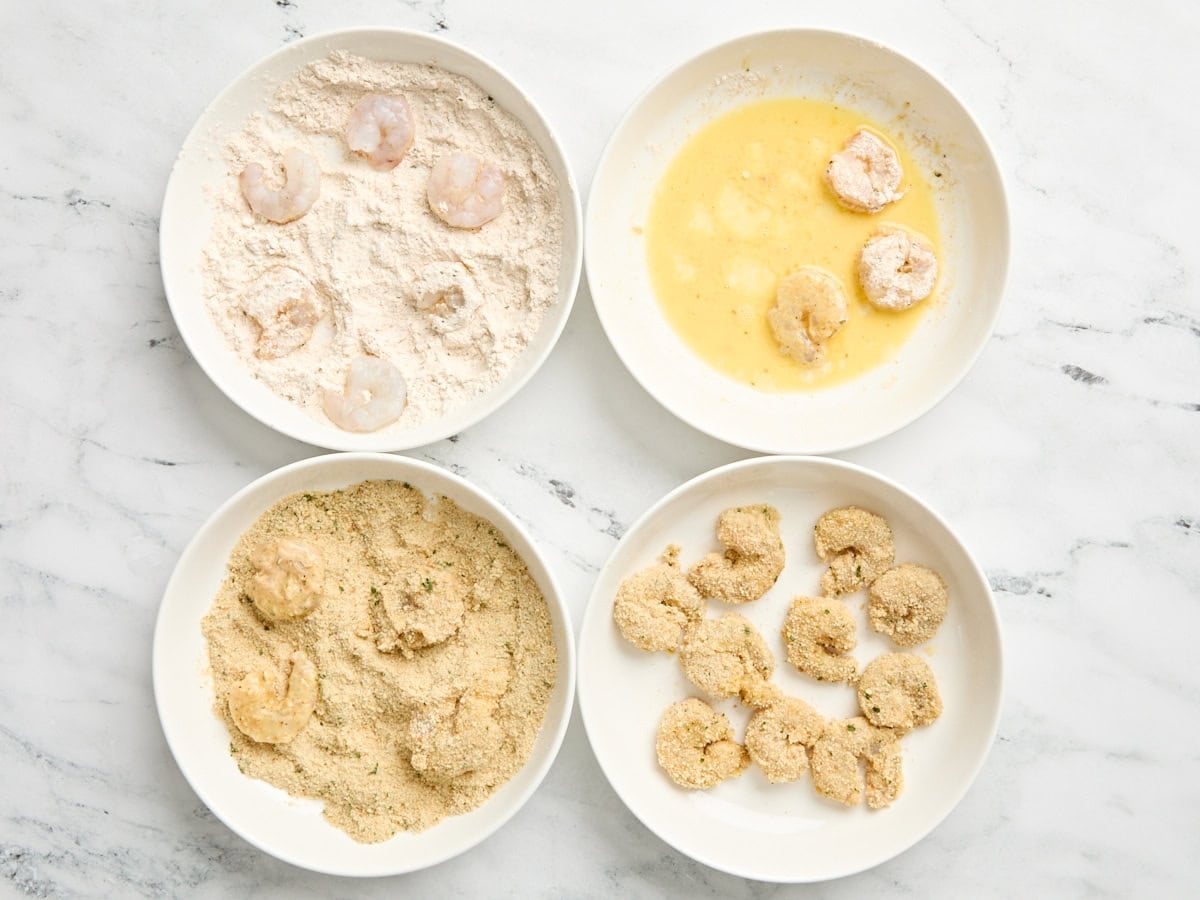 Raw shrimp being dipped in flour, then eff, then breadcrumbs,