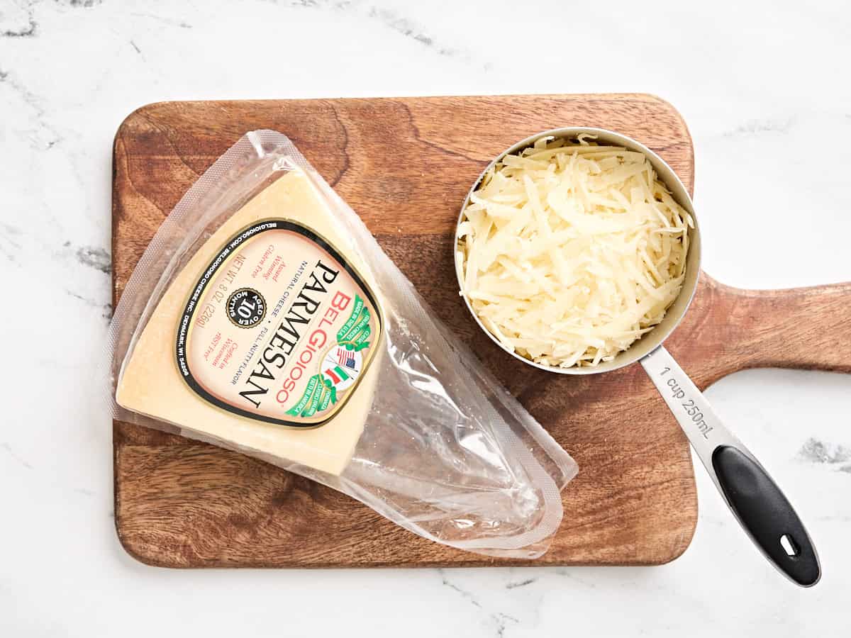 Grated parmesan cheese in a cup next to a parmesan wedge.