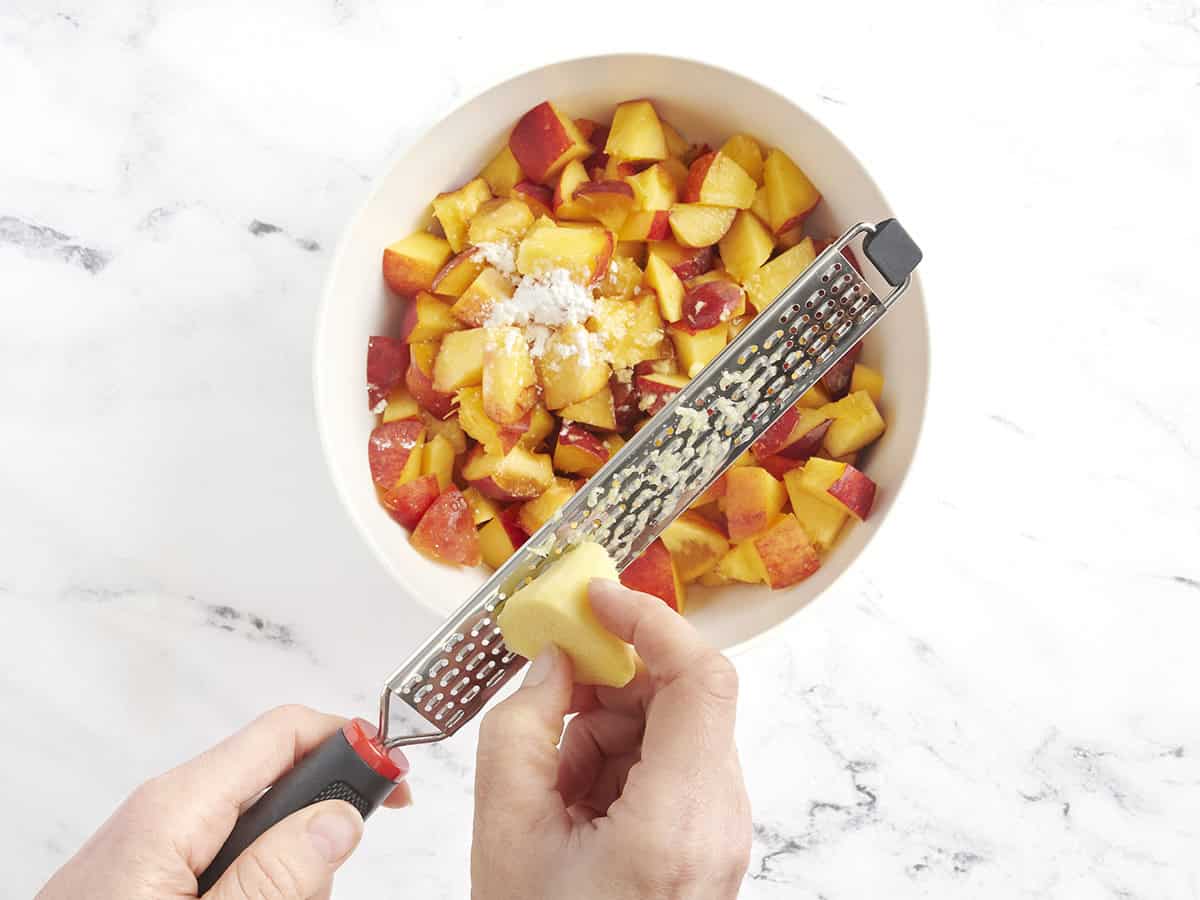 Ginger being grated into a bowl of peach slices and corn starch.