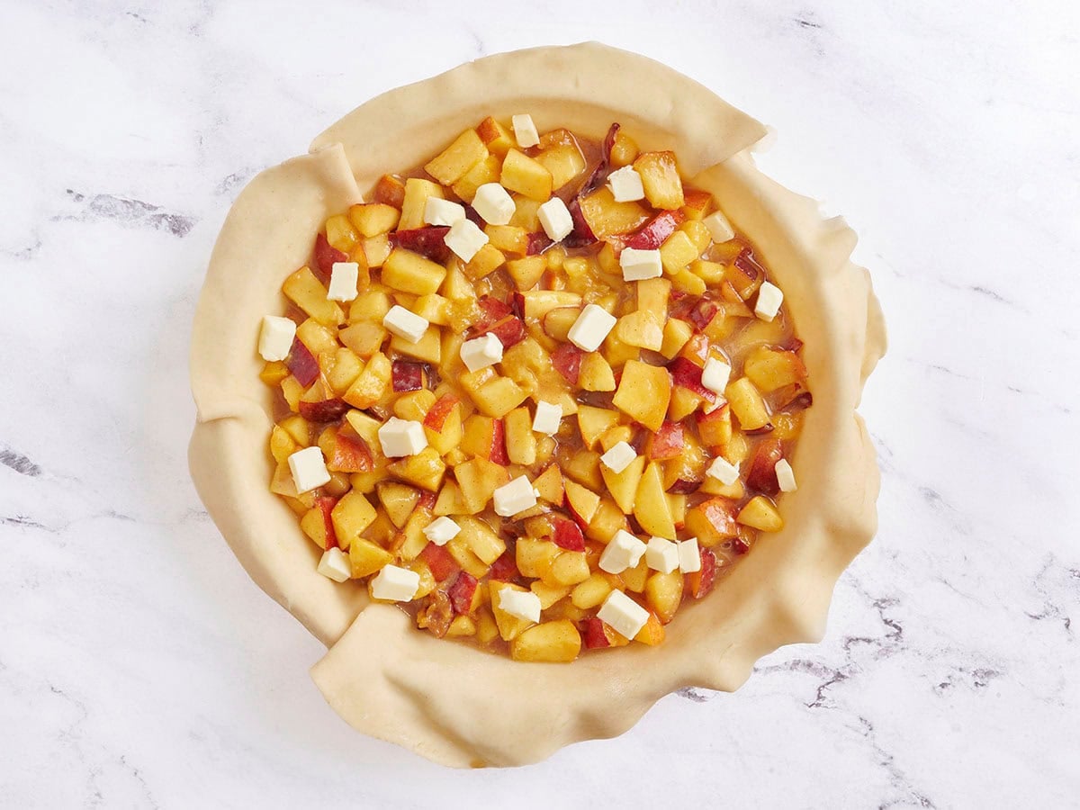 Peach pie filling in a pie dish topped with butter.