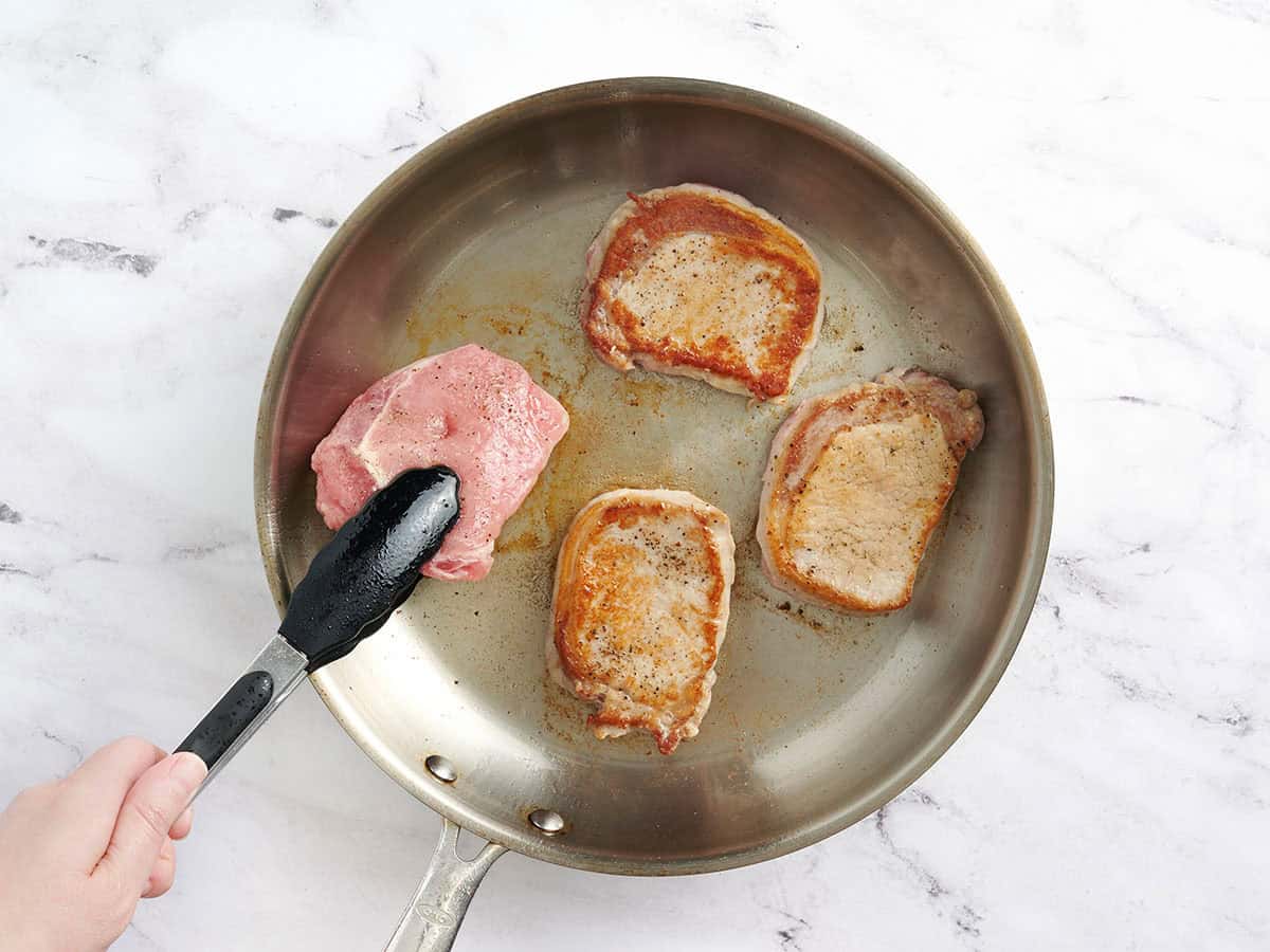 Pork chops being browned in a skillet.