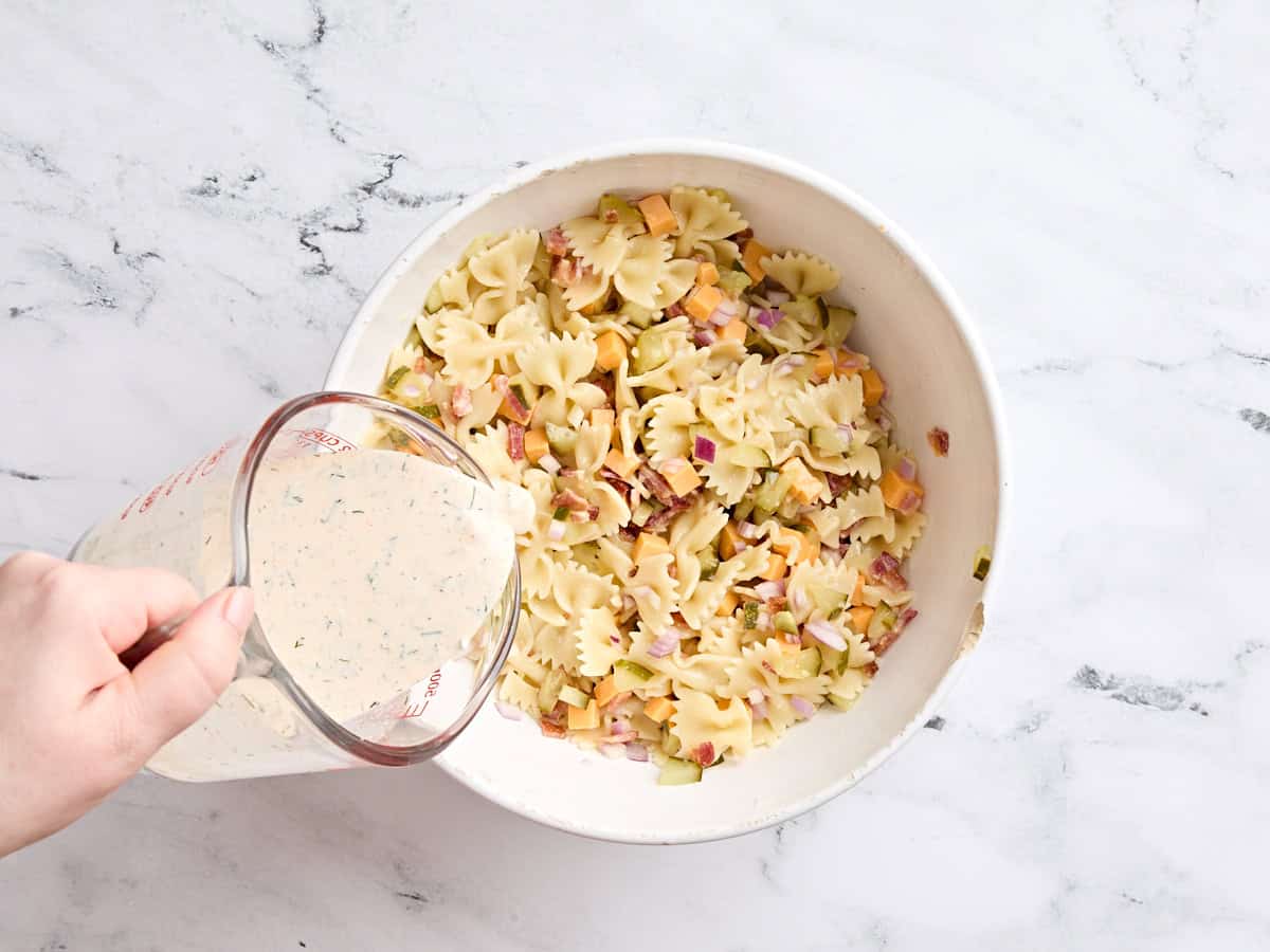 Homemade dressing being poured into a bowl of dill pickle salad.