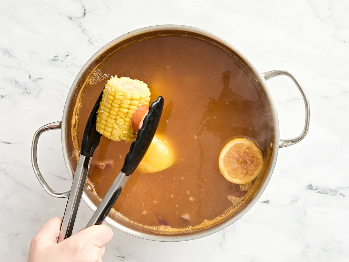 Corn cobs being added to a simmering pot of seasoned water.