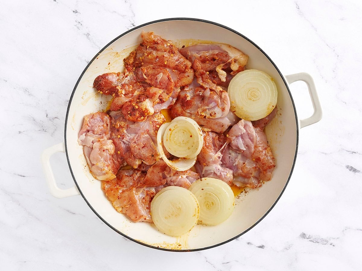 Seasoned chicken thighs added to browned onion halves in a skillet.