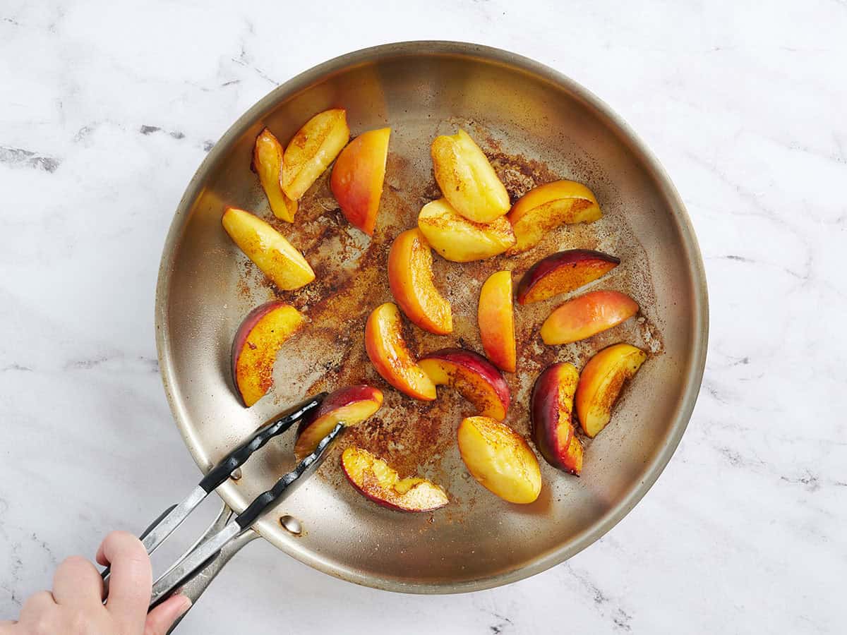 Peach wedges being browned in a skillet.