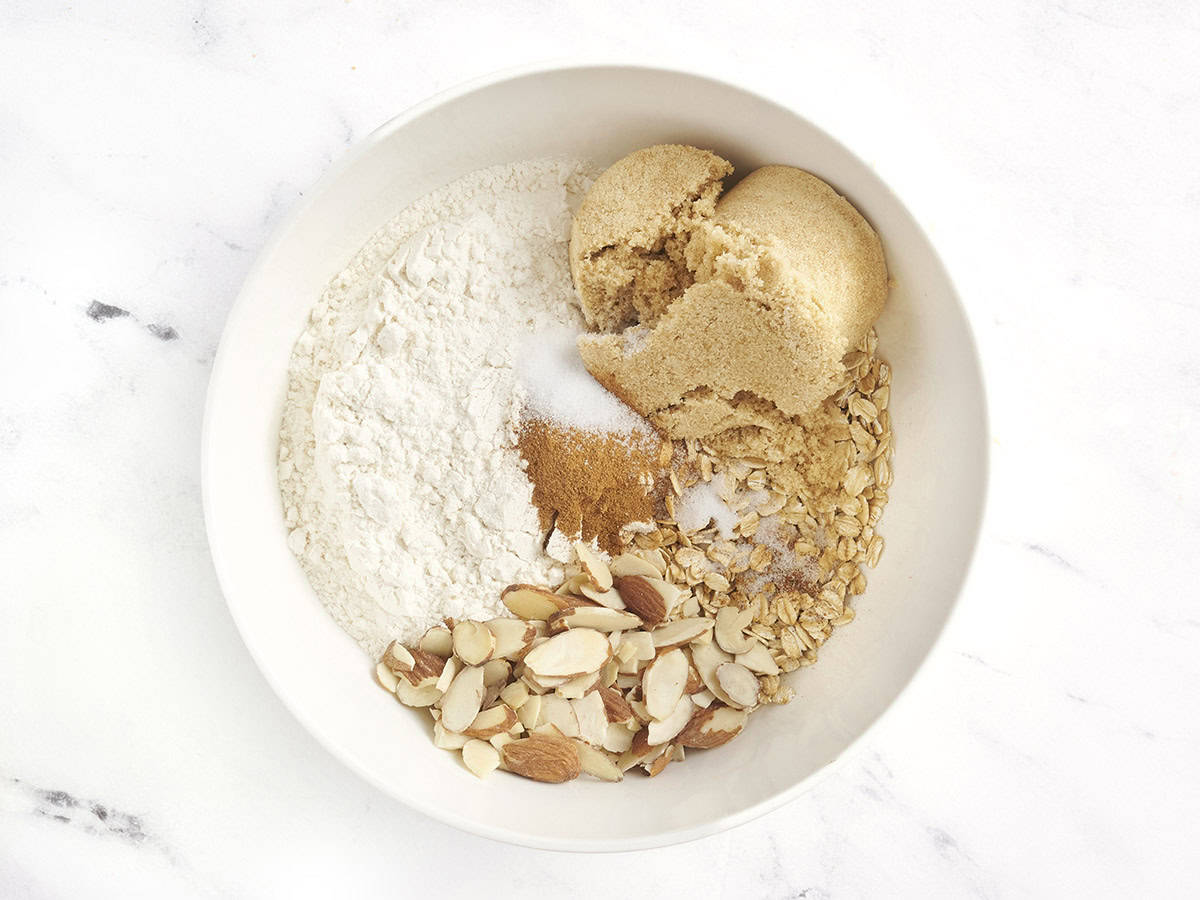 Flour, brown sugar, oats, sliced almonds, and cinnamon in a bowl.