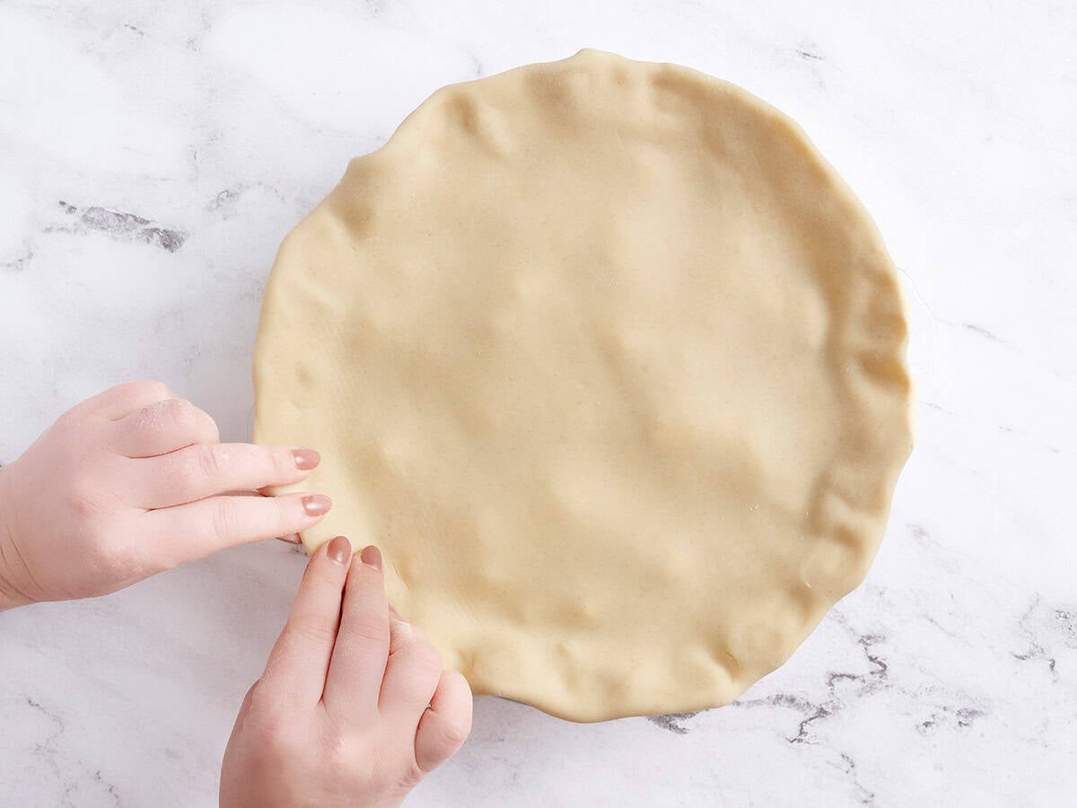 A hand crimping the top crust on a peach pie.