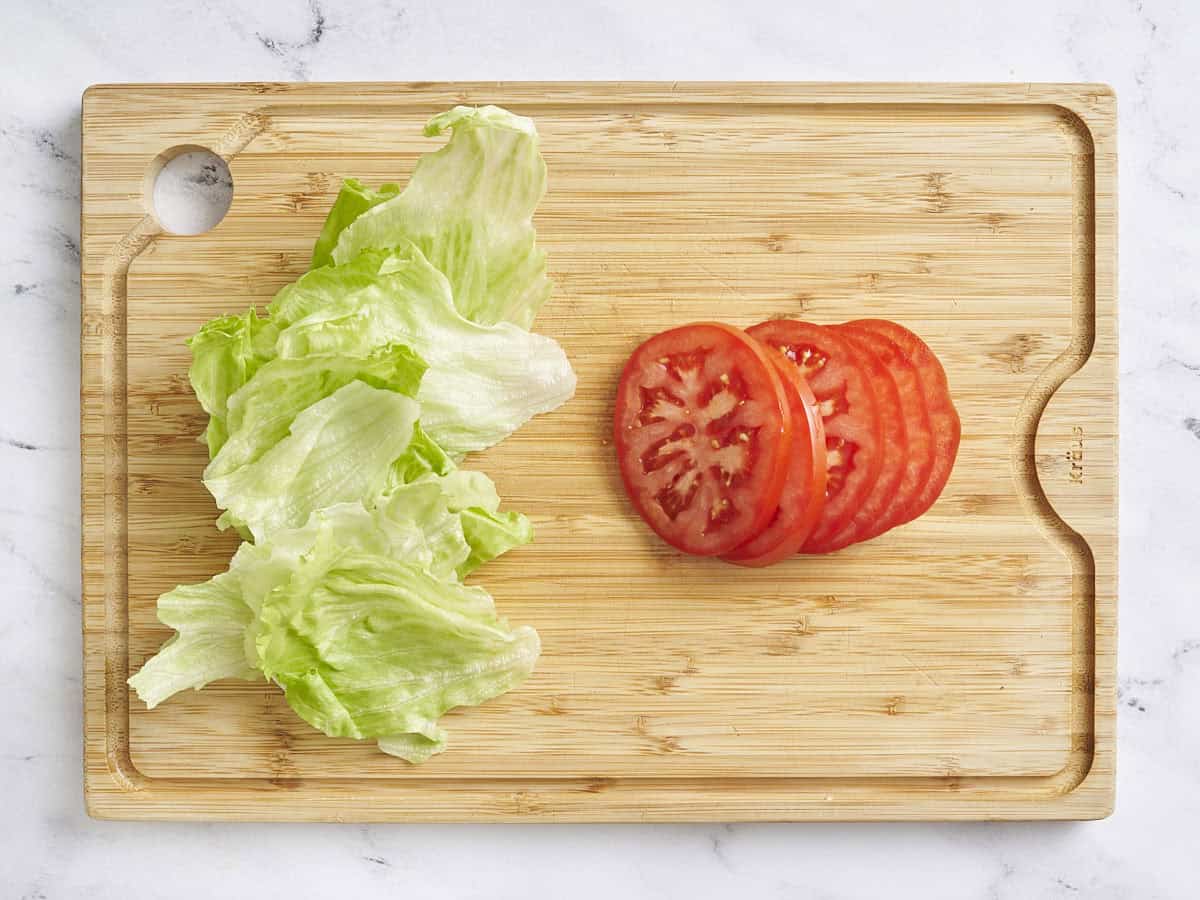 Sliced tomatoes and lettuce leaves on a wooden cutting board.