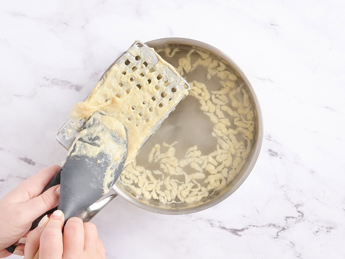 Spaetzle dough being pushed through a large grater.
