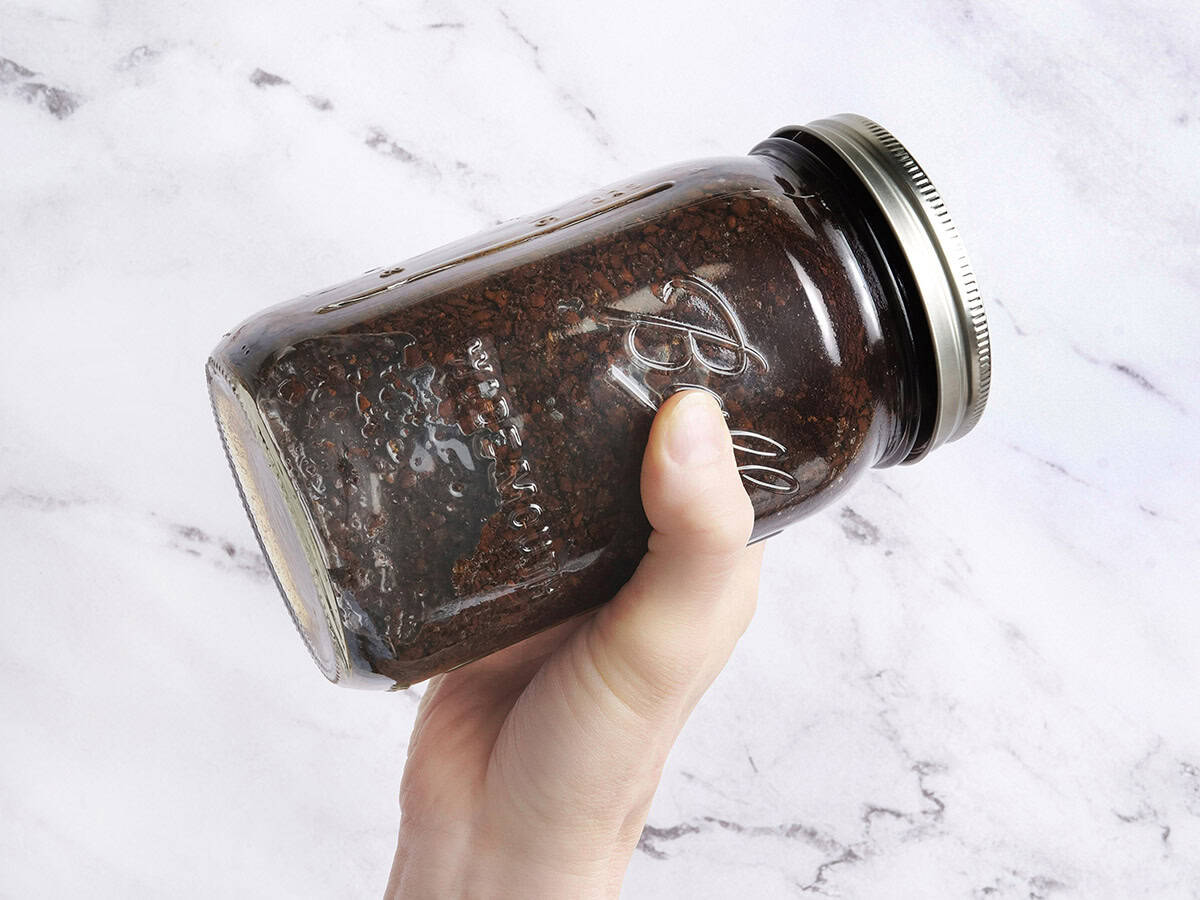 Ground coffee beans and water being shaken in a mason jar.