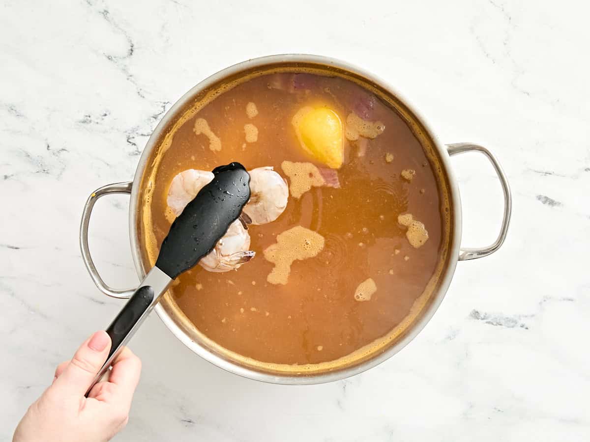 Shrimp being added to a simmering pot of seasoned water and potatoes.