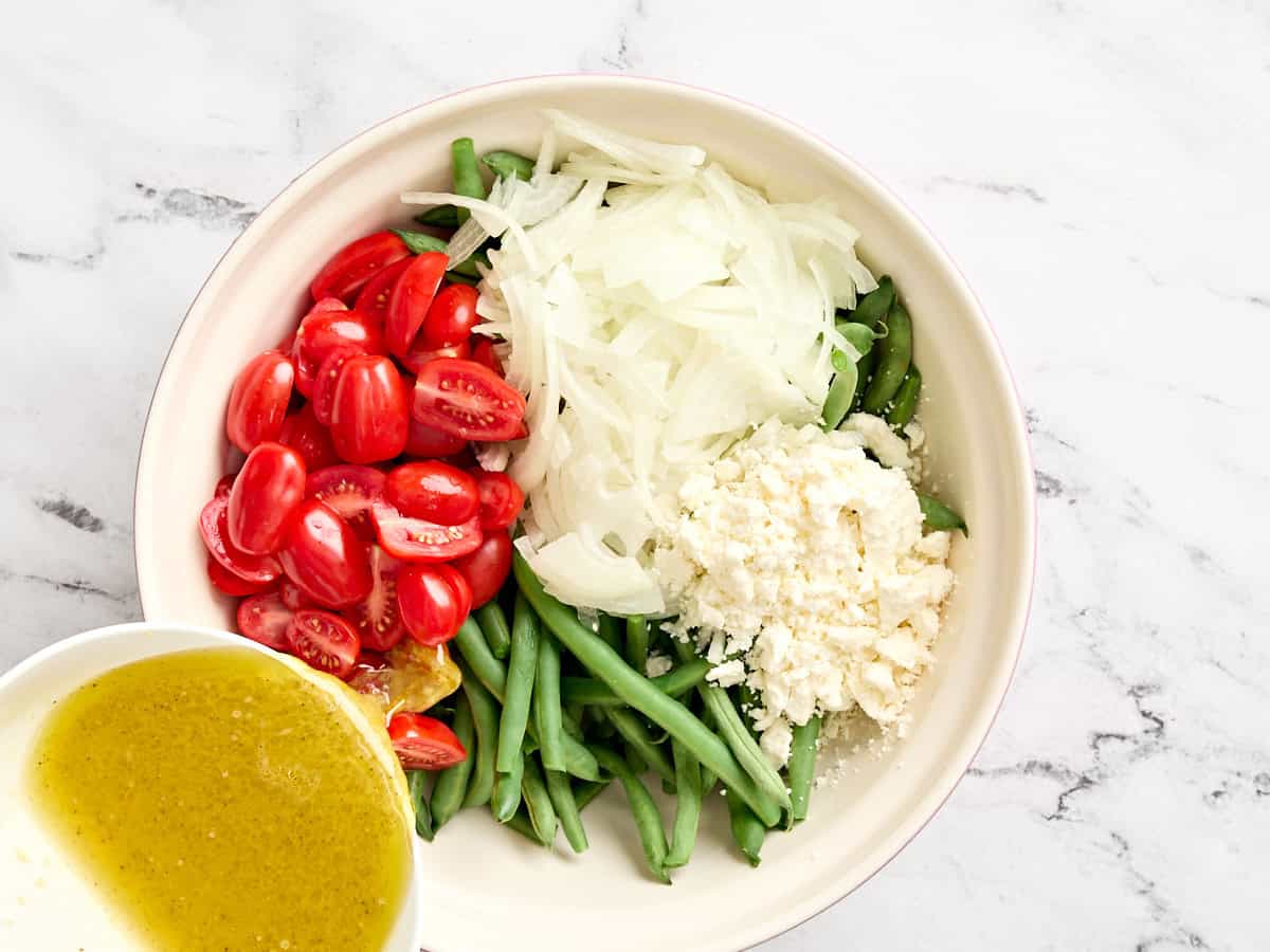 Chopped cherry tomatoes and onion added to a bowl of blanched green beans.