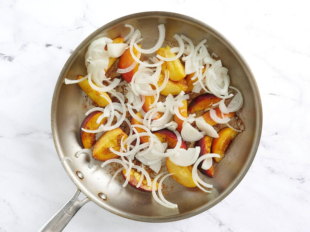 Sliced onion added to cooked peaches in a skillet.