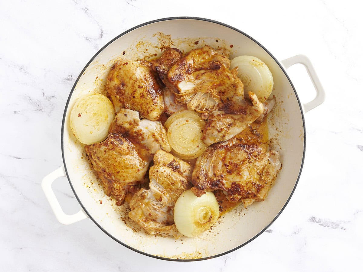 Browned chicken thighs and onion halves in a skillet.