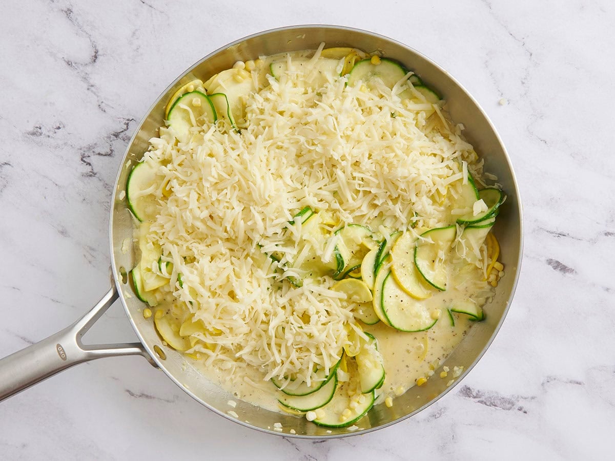 Shredded cheese added to a skillet with zucchini and yellow squash.