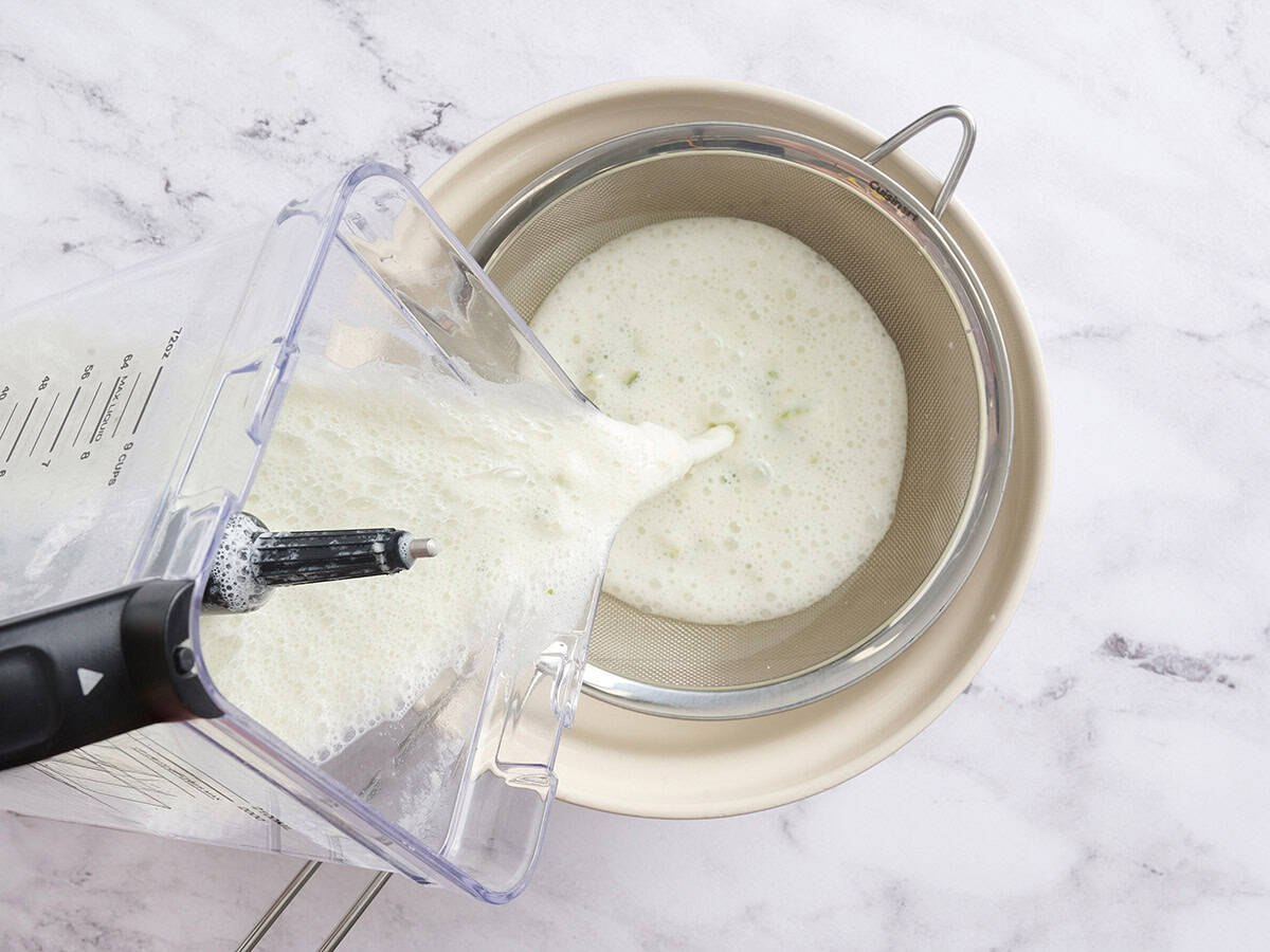 Brazilian lemonade being poured into a strainer over a bowl.