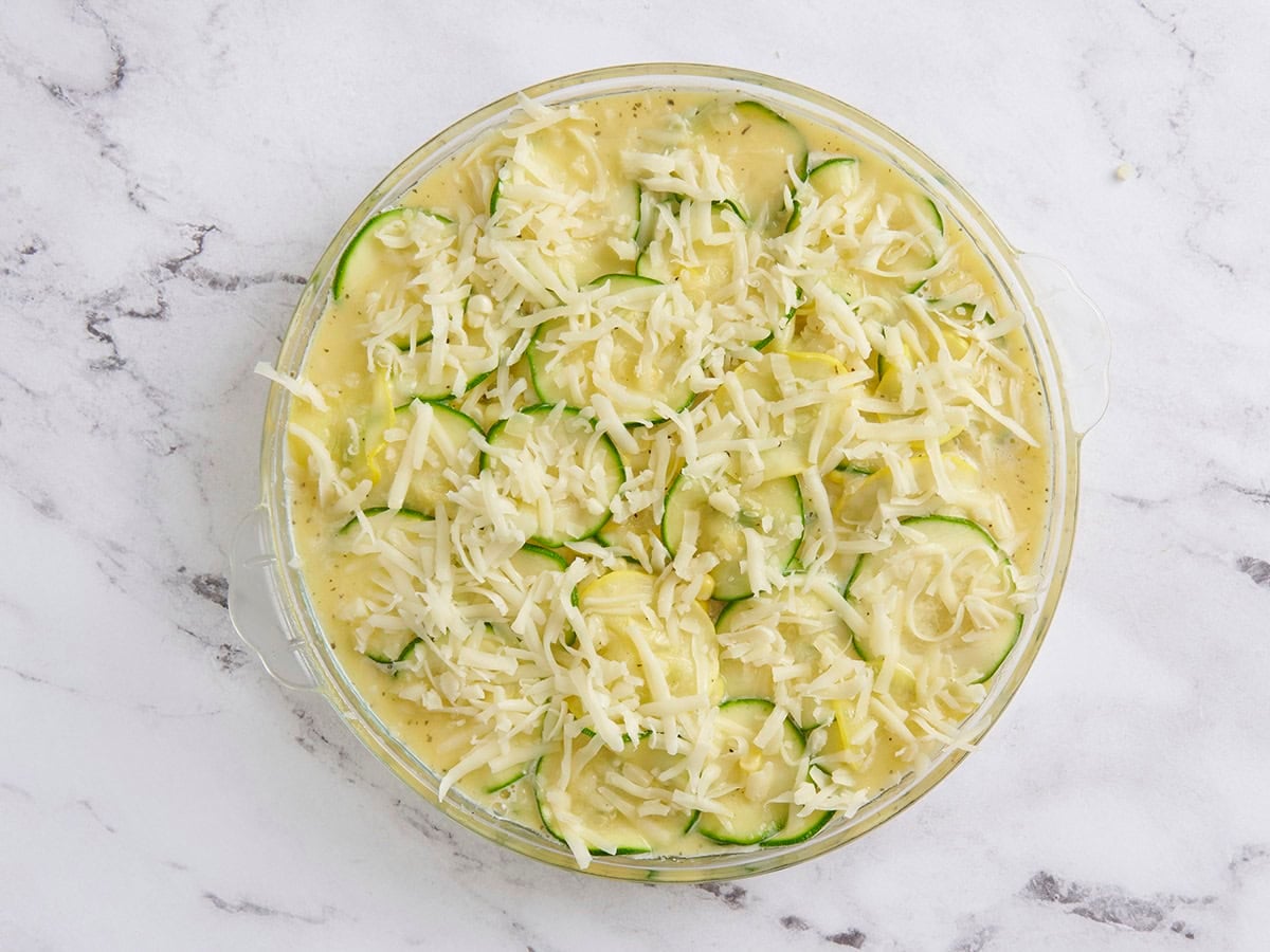 The ingredients for zucchini and corn pie in a skillet topped with shredded cheese.
