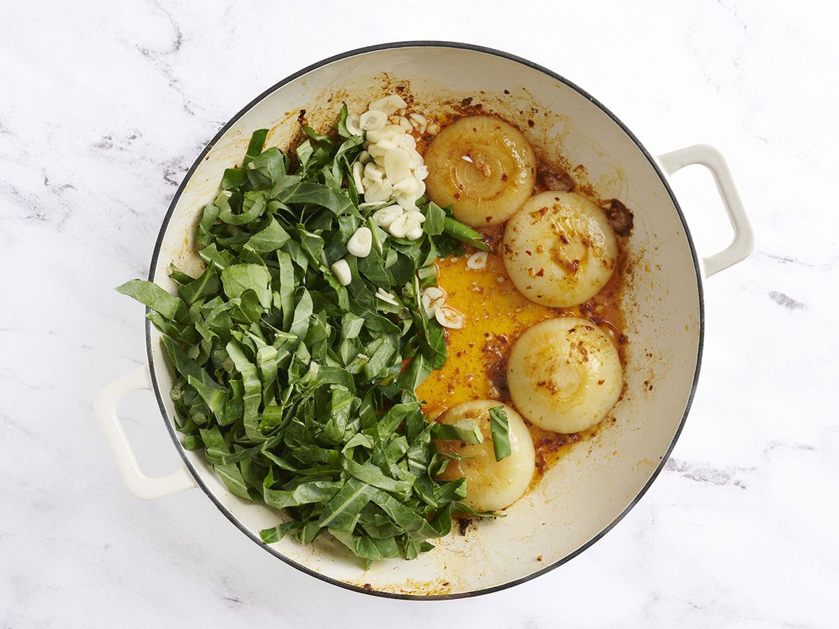 Collard greens and chopped garlic added to browned onion halves in a skillet.