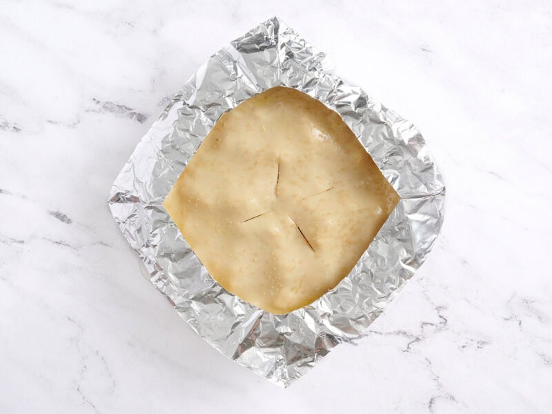 An unbaked homemade peach pie topped with a foil collar.