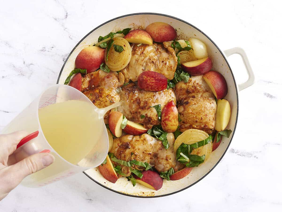Broth being added to Braised Chicken and Peaches in a skillet.