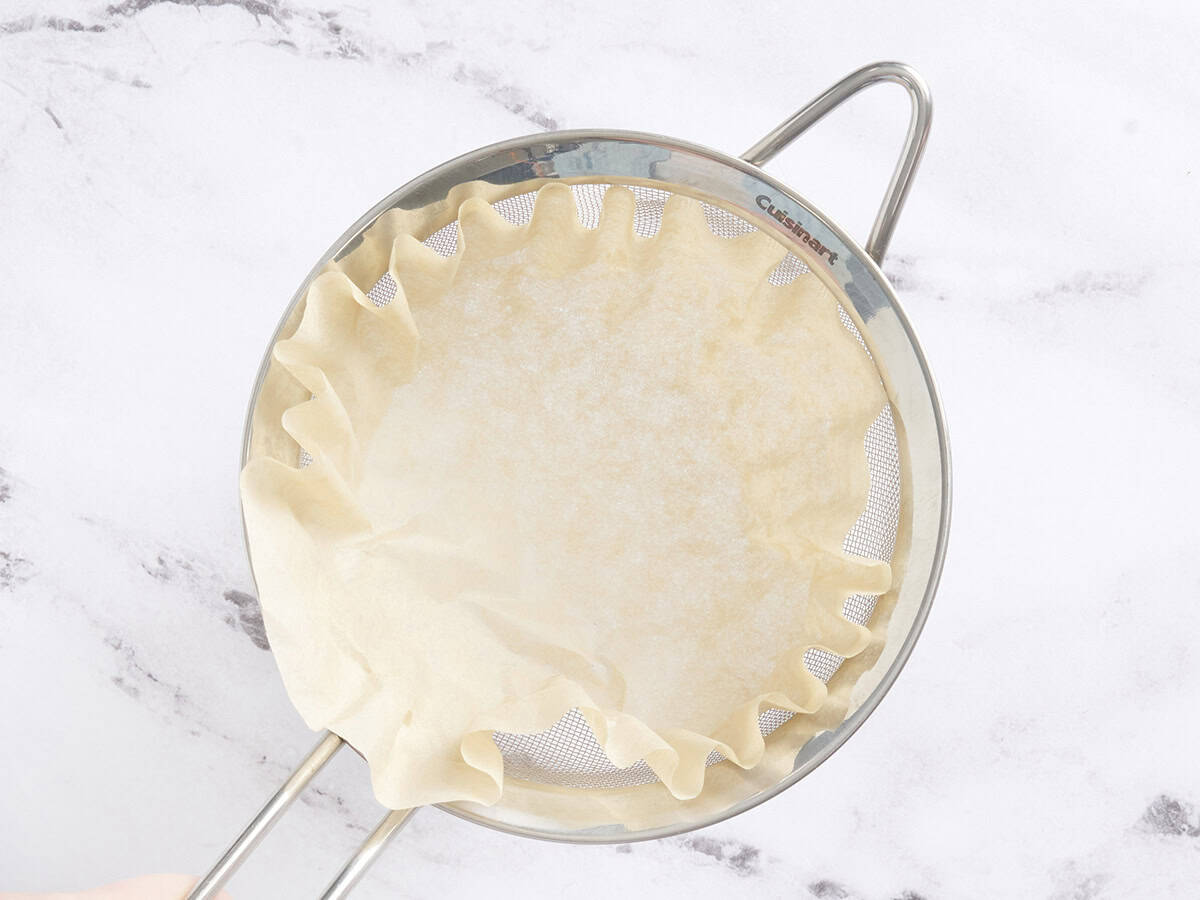A coffee strainer in a metal strainer over a bowl.