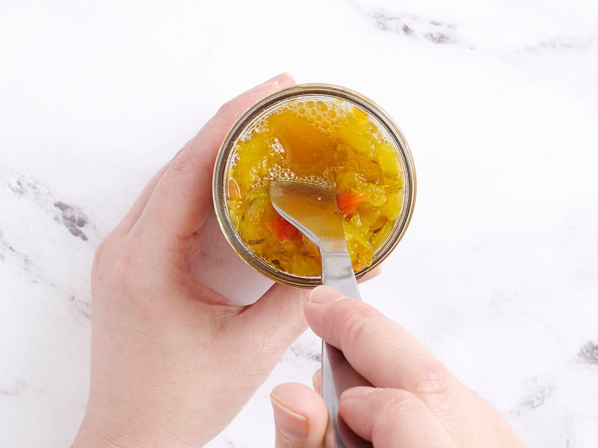 A fork pushing down zucchini relish in a jar so the liquid rises to the top.