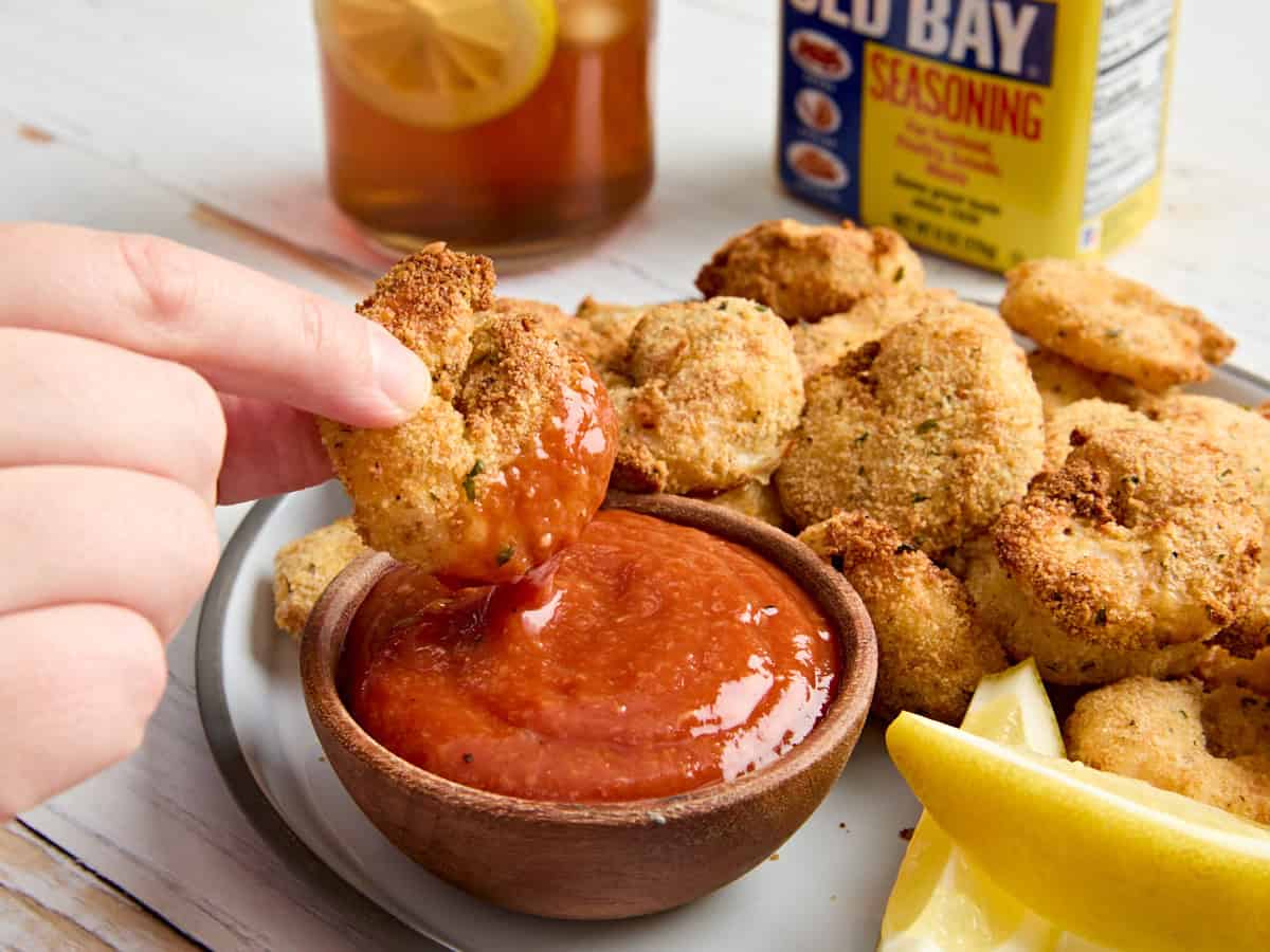 A hand dipping an air fried fried shrimp into cocktail sauce.