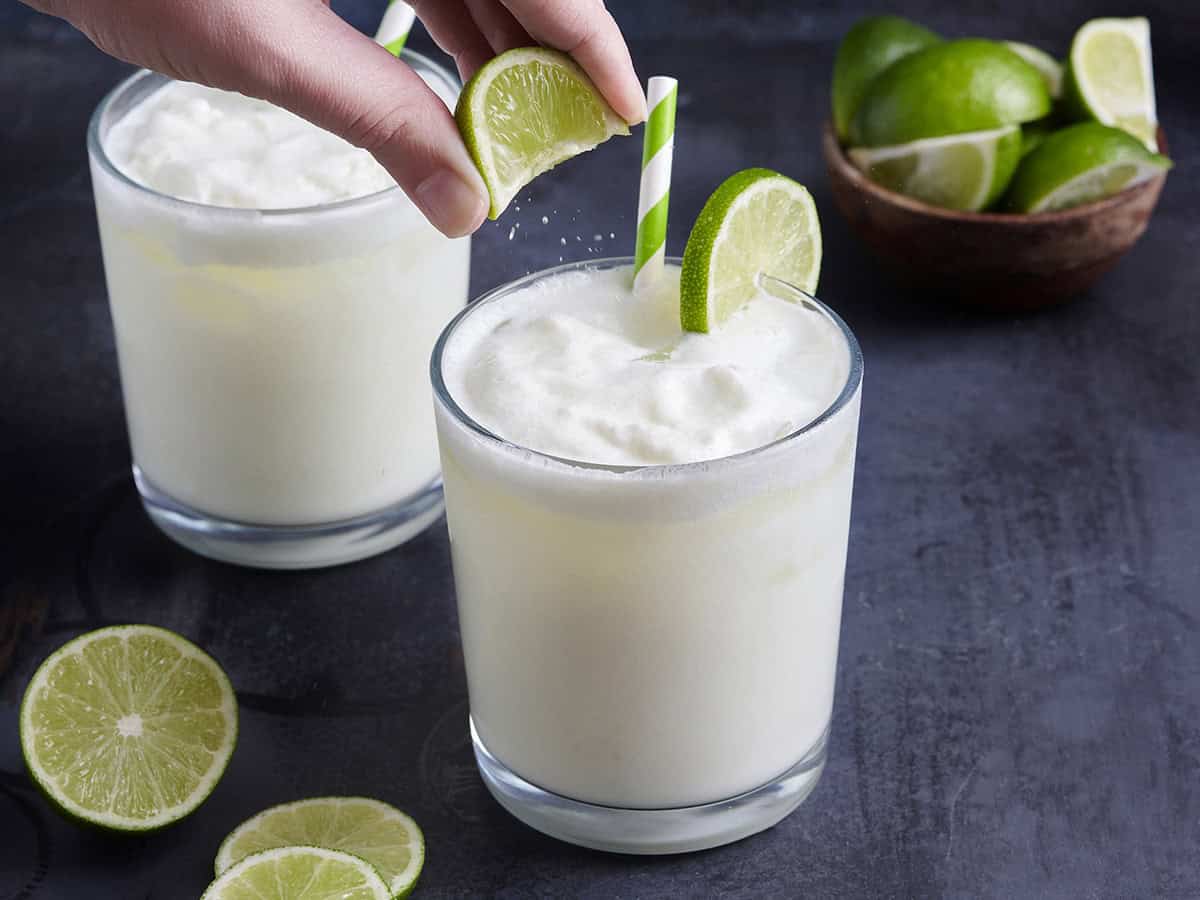 A hand squeezing a wedge of lime over a glass of Brazilian lemonade.