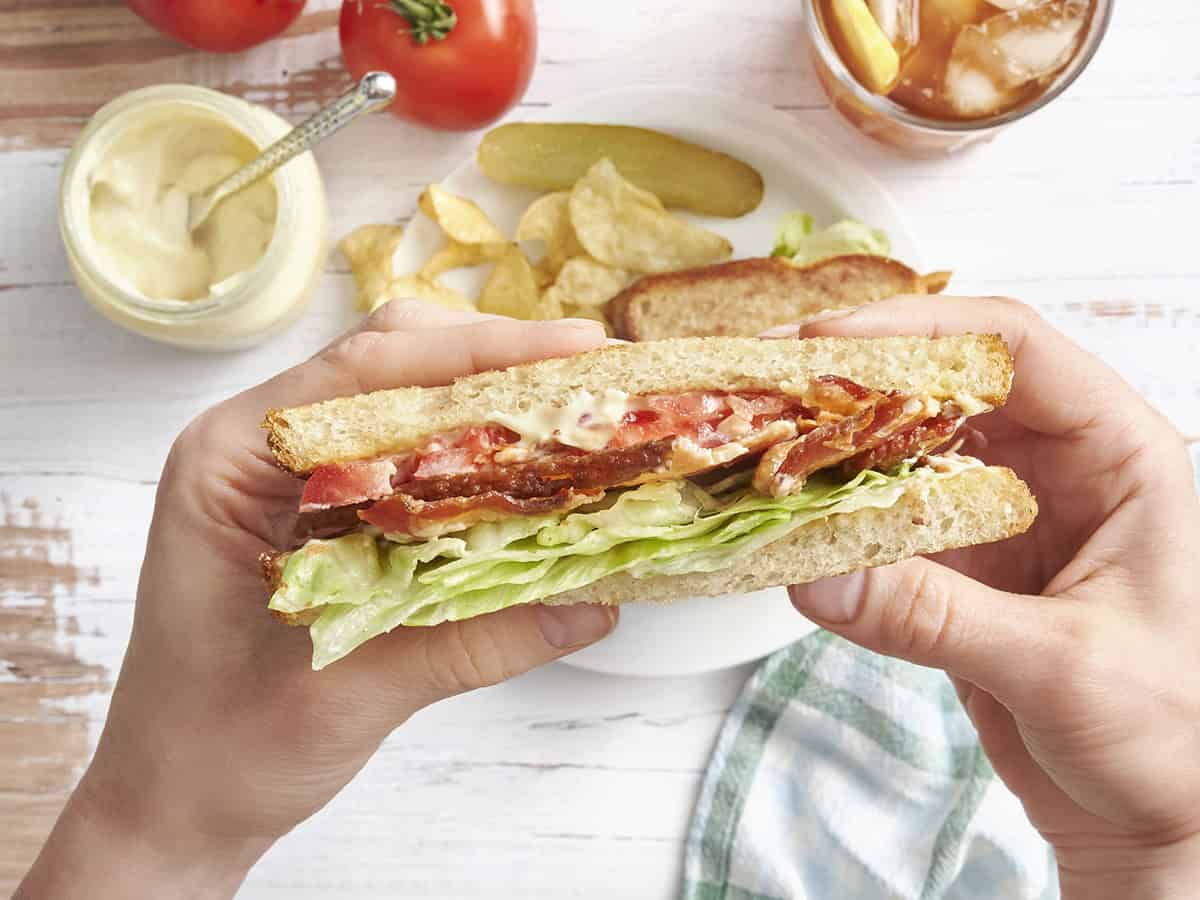 Overhead view of hands holding a blt sandwich.