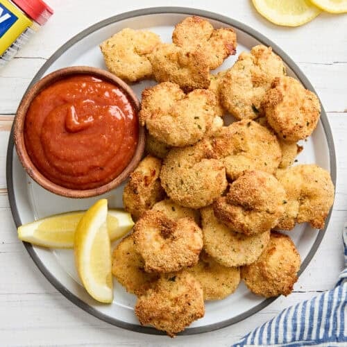 Overhead view of a bowl of cocktail sauce on a plate with fried shrimp.