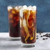 Side view of two glassed of cold brew coffee with ice, one with cream added.