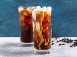 Side view of two glassed of cold brew coffee with ice, one with cream added.