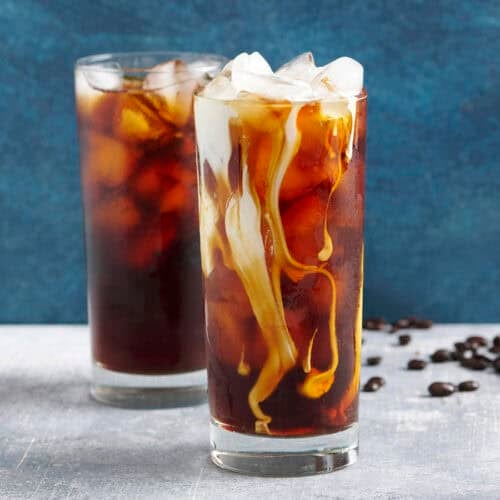 Side view of two glassed of cold brew coffee with ice, one with cream added.