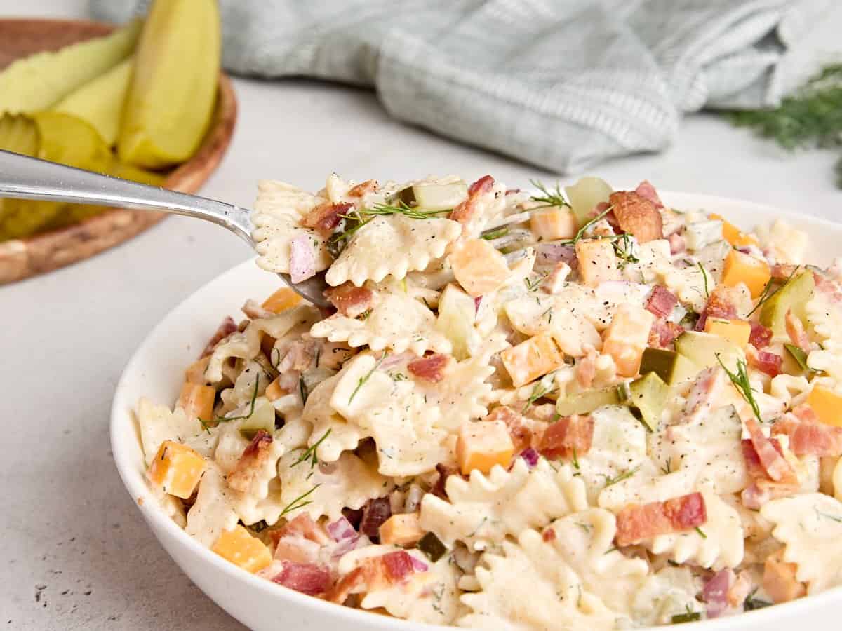 Side view of a bowl of creamy pickle pasta salad with a fork taking some.
