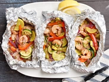 Overhead view of grilled shrimp and vegetable foil packets on a serving platter.