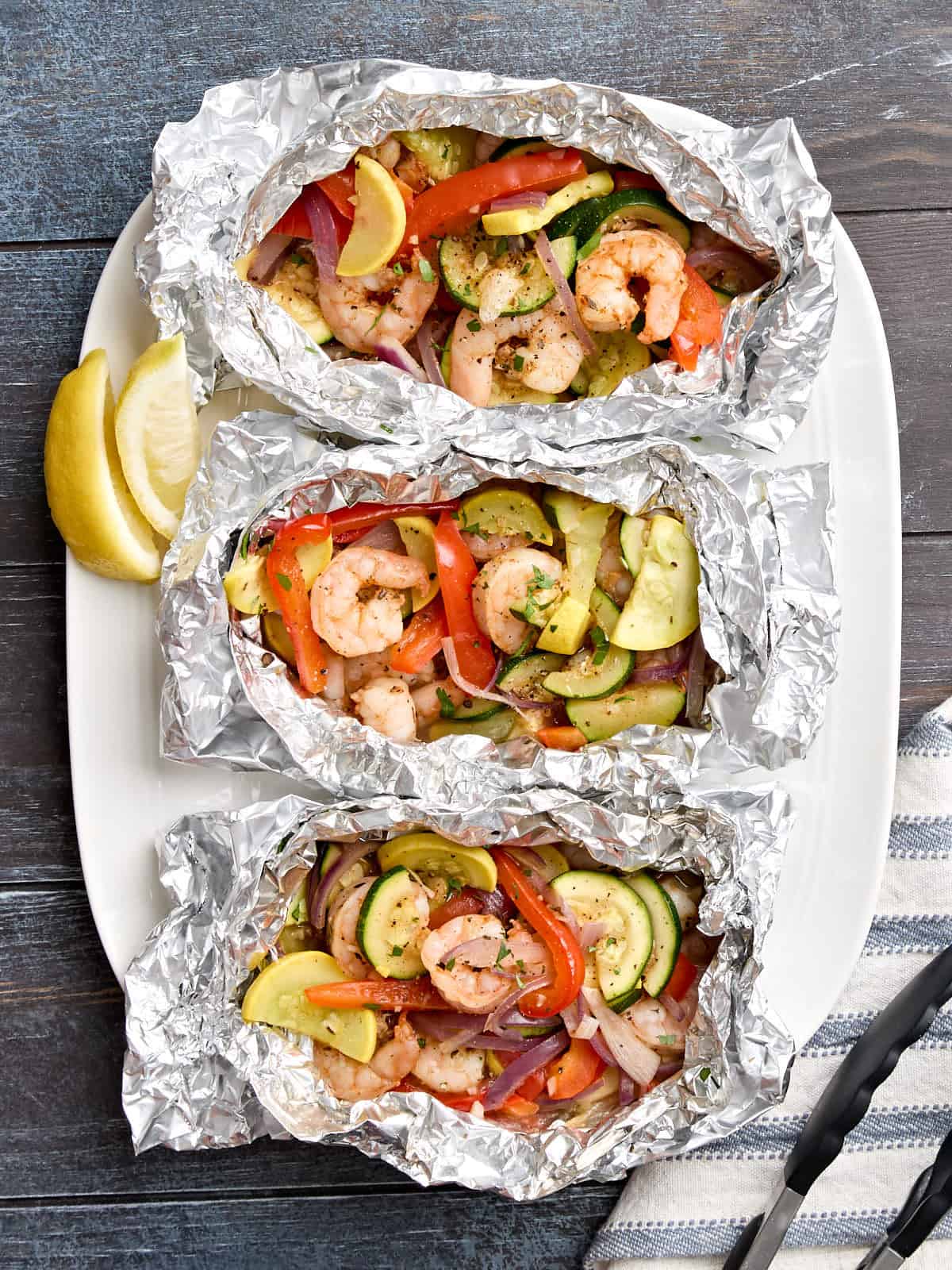 Overhead view of grilled shrimp and vegetable foil packets on a serving platter.