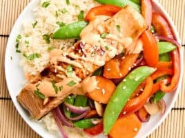 Overhead view of teriyaki salmon on a plate with stir fried vegetables and rice.