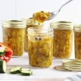 Side view of jars of zucchini relish, is a spoon taking some from one jar.